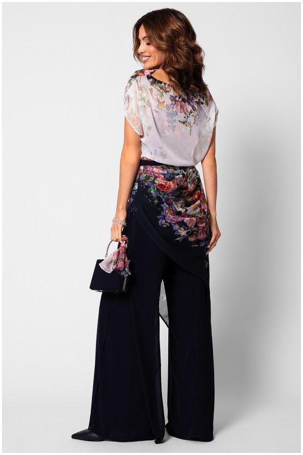 Woman wearing the floral-overall-tina-two-layer with floral top and navy flared trousers, holding a matching handbag.