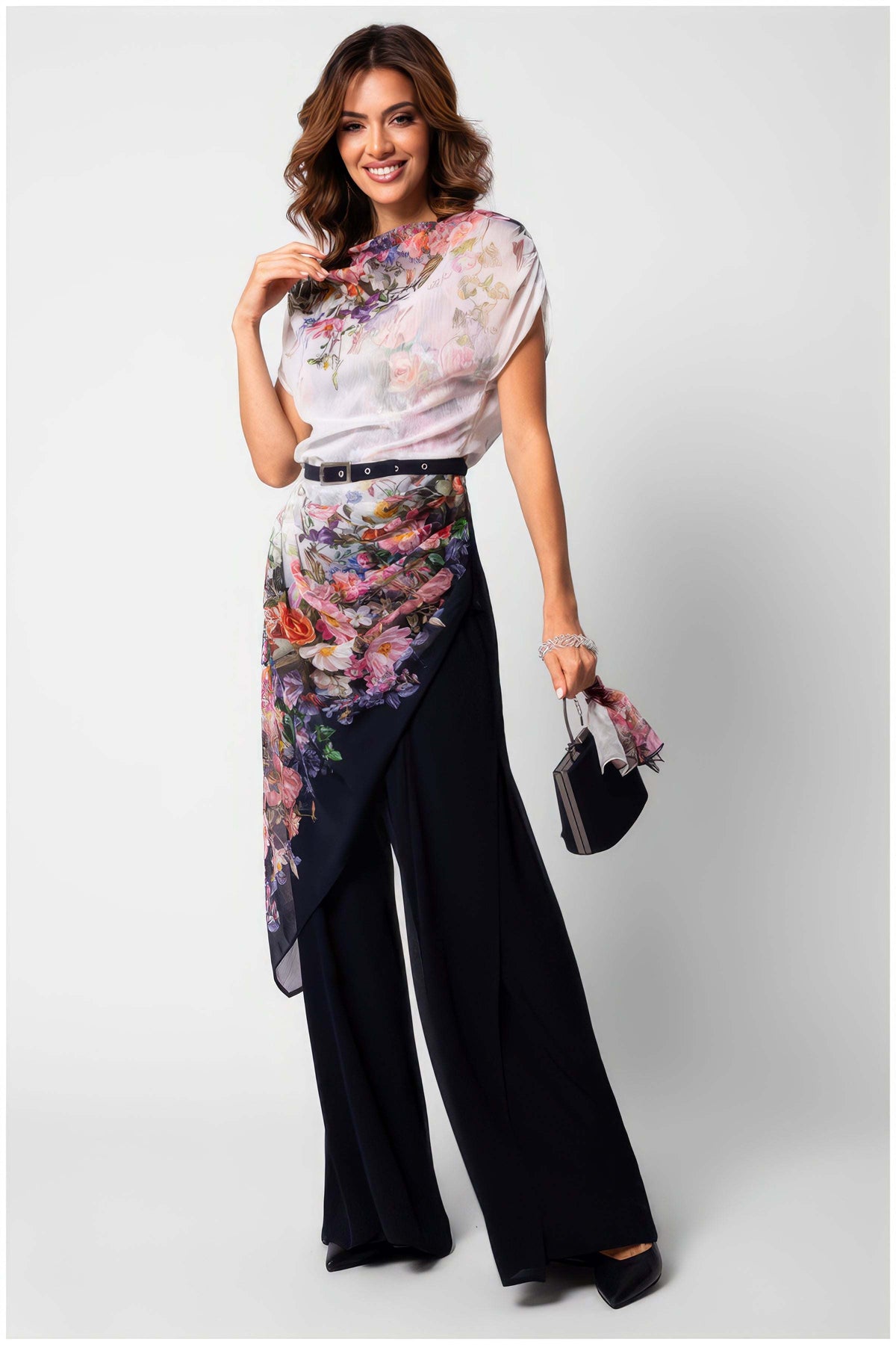 Navy Floral Two Layer Jumpsuit, Tina. Jumpsuit. Sheer white overlay with a pink and purple floral print draped from a high neckline over navy wide-leg pants, with a slim dark belt, on model.