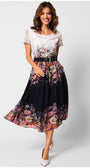 Woman wearing elegant midi dress Julia Dress with floral pattern, black belt, flowing midi length, and white pointed shoes on white background.