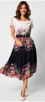 Woman wearing elegant midi dress Julia Dress with floral pattern, black belt, flowing midi length, and white pointed shoes on white background.