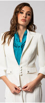 Woman wearing a fitted white tailored blazer with three-quarter sleeves and a teal scarf in a studio setting