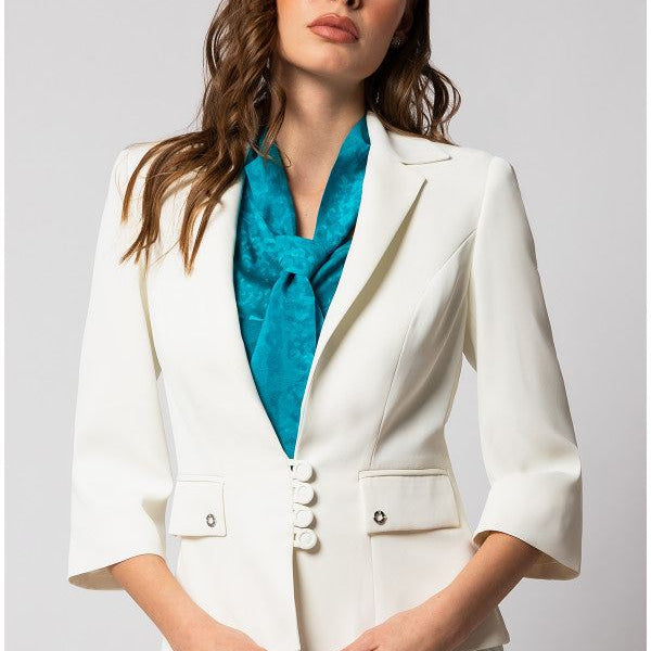 Woman wearing a fitted white tailored blazer with three-quarter sleeves and a teal scarf in a studio setting