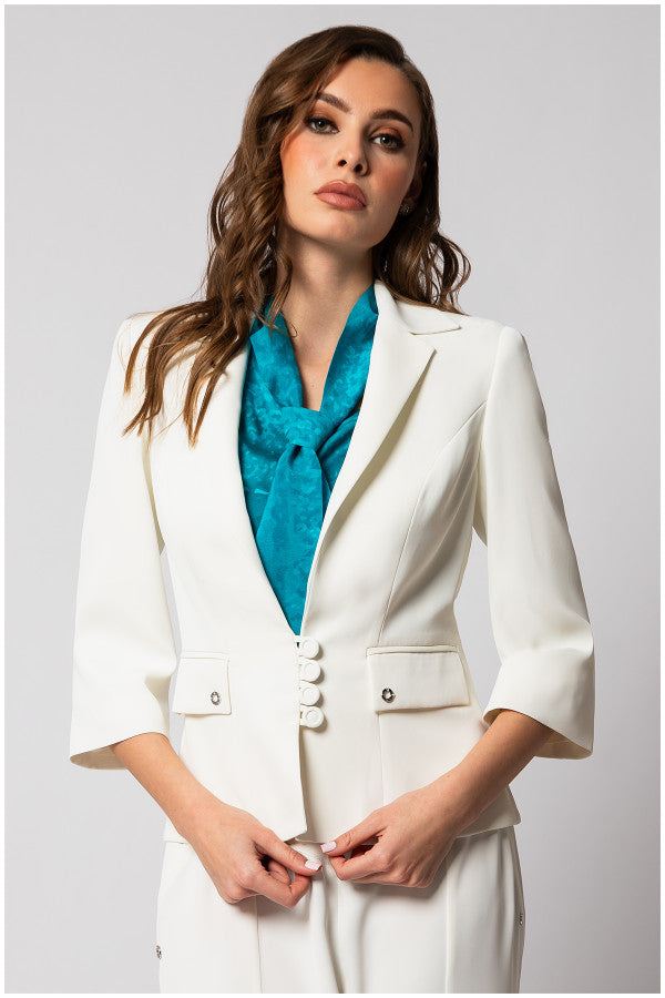 Woman wearing a fitted white tailored blazer with three-quarter sleeves and a teal scarf in a studio setting