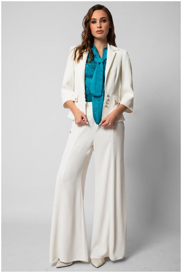 Woman wearing a white tailored blazer with wide-leg trousers and teal blouse featuring a bow tie neck detail.