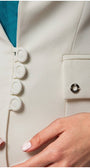 Close-up of white fitted blazer with covered buttons and tailored pocket detail on sleeve cuff.