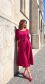 Pink Elegant Midi Dress, Charlotte. Worn beside a stone wall, side view.