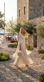Rebeka ivory cape-sleeve gown worn on a sunlit stone harbor walkway