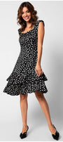 Woman wearing a fitted ruffle satin dress with white polka dots and tiered ruffle hem, smiling and posing standing.