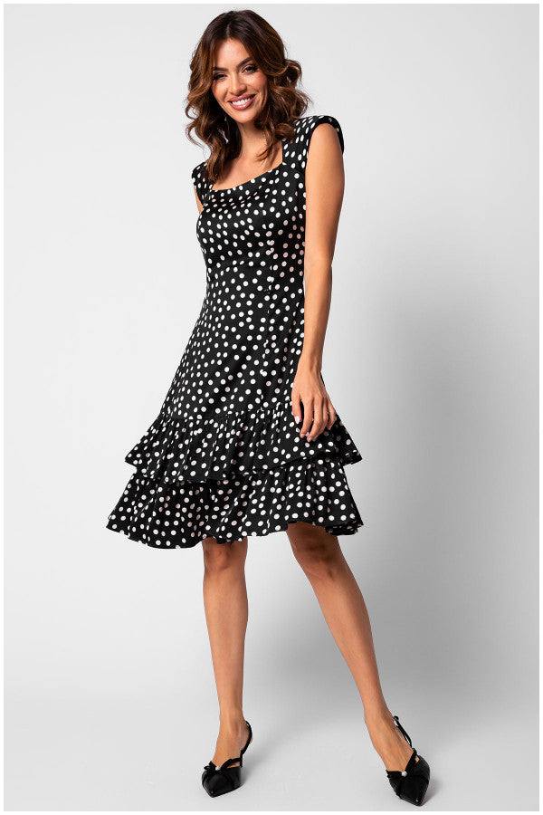 Woman wearing a fitted ruffle satin dress with white polka dots and tiered ruffle hem, smiling and posing standing.