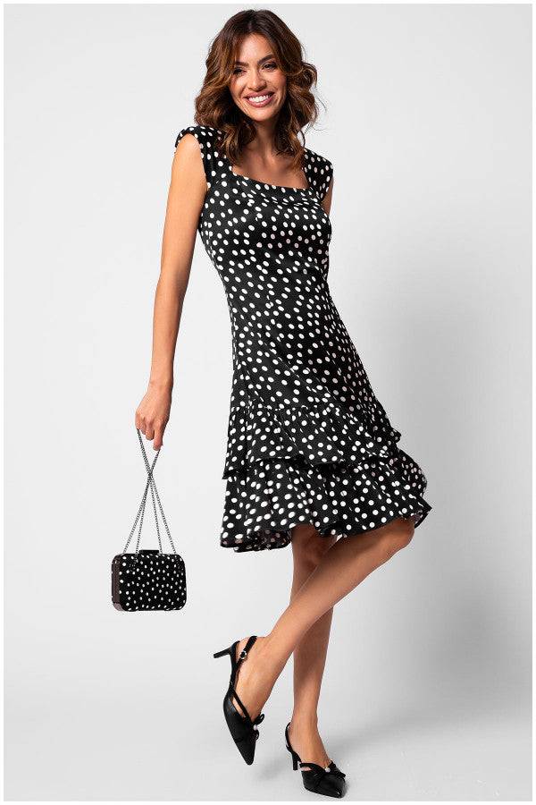 Woman wearing a black and white polka-dot ruffle satin dress hem holding matching purse and black heels