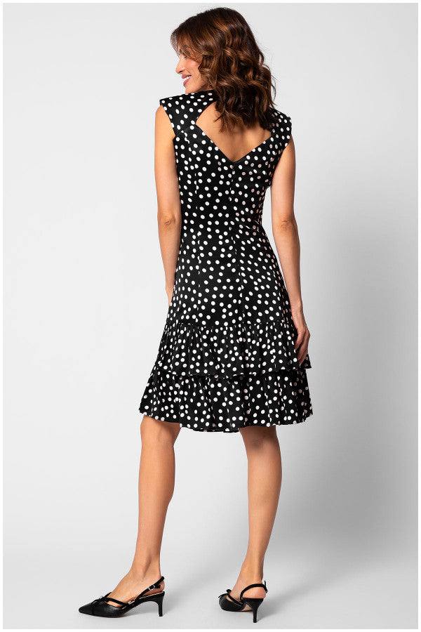 Woman wearing a black and white polka-dot fitted satin dress with tiered ruffle hem and V-back detail