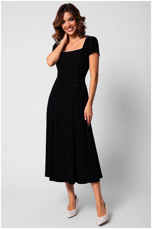 Smiling woman wearing a black elegant midi dress with a square neckline and short sleeves, posing on a light background