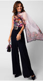 Woman wearing a silk floral scarf Loretta Scarf draped elegantly over shoulders with black wide-leg trousers and matching handbag accessory.