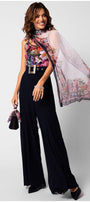Woman wearing a silk floral scarf Loretta Scarf draped elegantly over shoulders with black wide-leg trousers and matching handbag accessory.