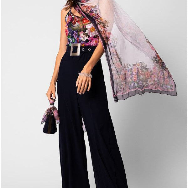 Woman wearing a silk floral scarf Loretta Scarf draped elegantly over shoulders with black wide-leg trousers and matching handbag accessory.