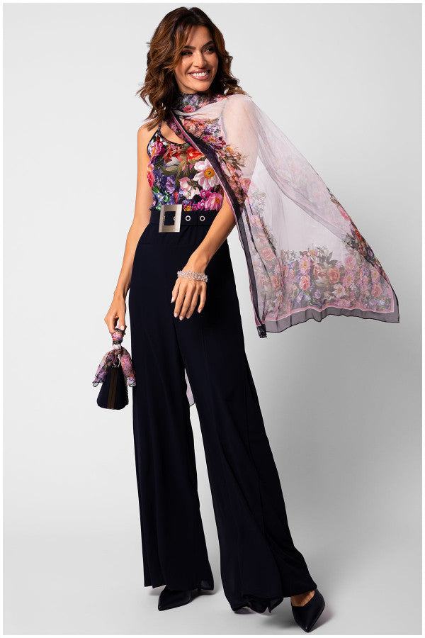 Woman wearing a silk floral scarf Loretta Scarf draped elegantly over shoulders with black wide-leg trousers and matching handbag accessory.