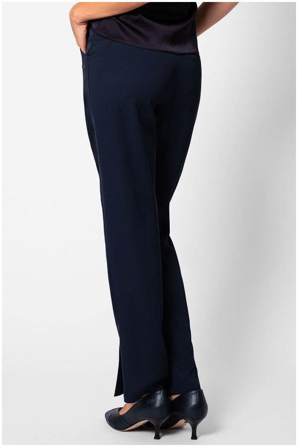 Woman wearing navy women travel pants Teodora pants with a straight-leg cut and black heels on a white background