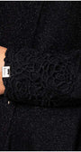 Close-up of black lace cardigan Jody lace cuff with intricate floral design and Luna brand tag on sparkly fabric background