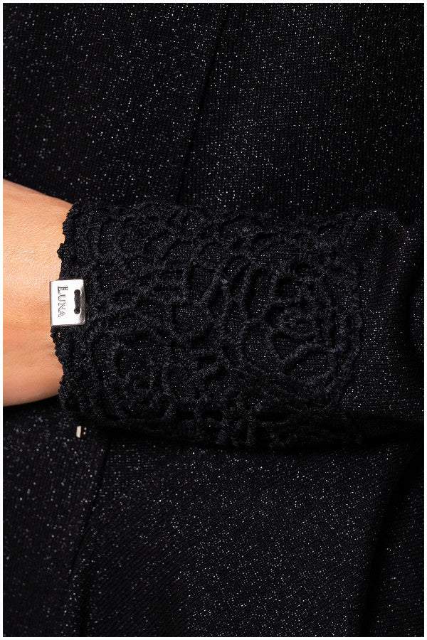 Close-up of black lace cardigan Jody lace cuff with intricate floral design and Luna brand tag on sparkly fabric background