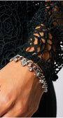 Close-up of hand wearing silver charm bracelet with floral lace sleeve in midnight green sweater Jody