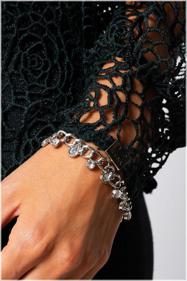 Close-up of hand wearing silver charm bracelet with floral lace sleeve in midnight green sweater Jody