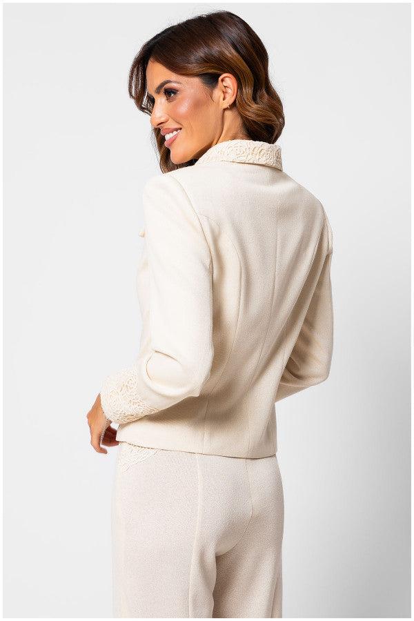 Woman wearing an ivory lace-embroidered tailored blazer Jody with a tailored waist and matching trousers, posing sideways.