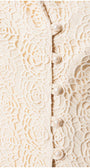 Close-up of ivory lace fabric with floral embroidery and pearl buttons on a delicate tailored blazer front closure.