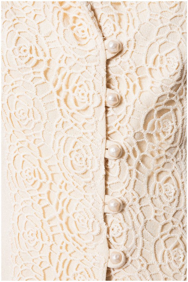 Close-up of ivory lace fabric with floral embroidery and pearl buttons on a delicate tailored blazer front closure.