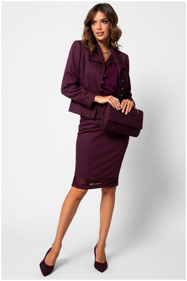 Woman wearing a bordeaux lace elegant blouse under blazer and skirt set with lace details, holding a matching handbag and wearing pointed heels.