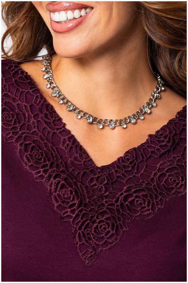 Close-up of a woman wearing the bordeaux lace elegant blouse  Top Jody with intricate lace neckline detail and a silver charm necklace.