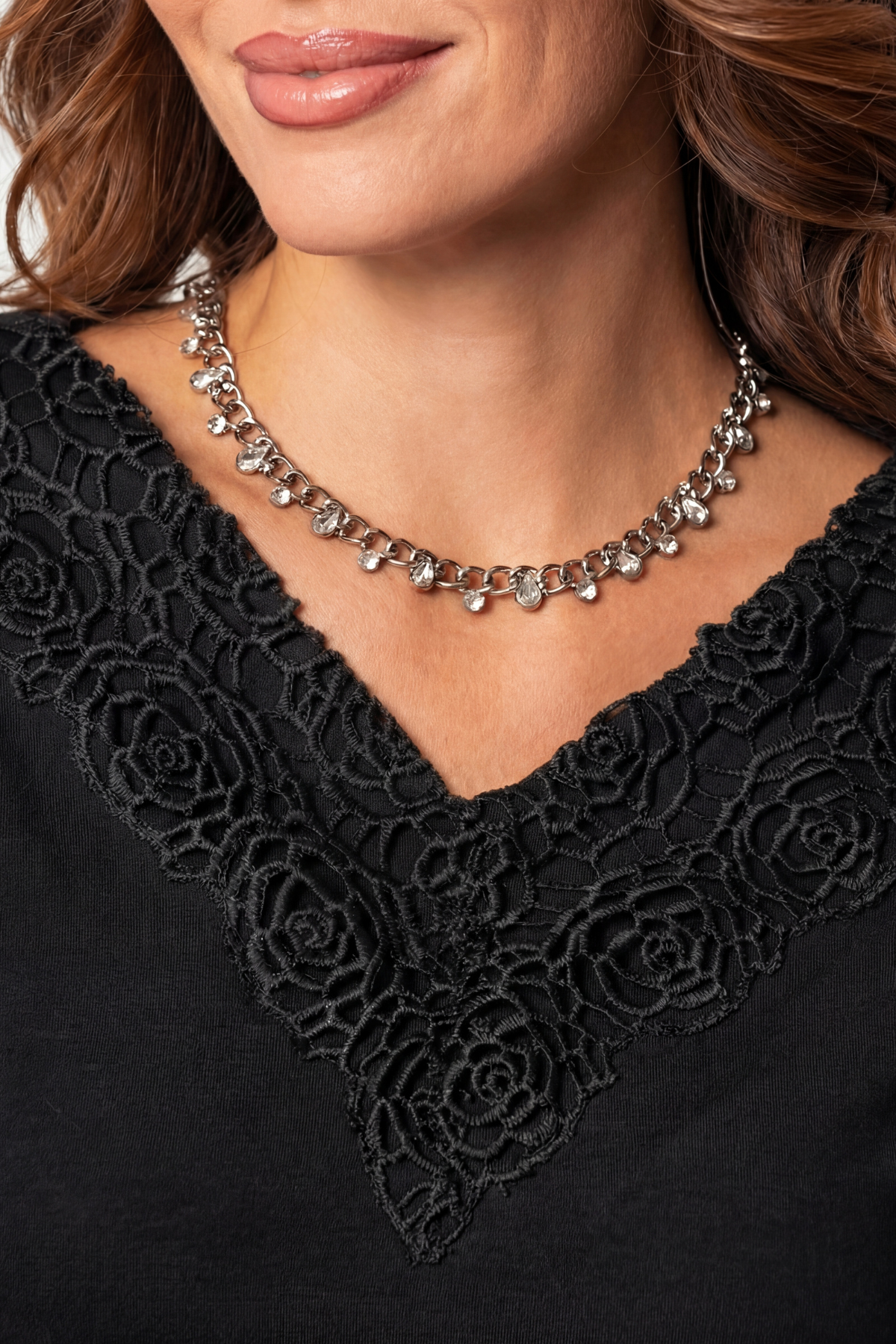 Close-up of a person wearing a black lace garment and a silver necklace.