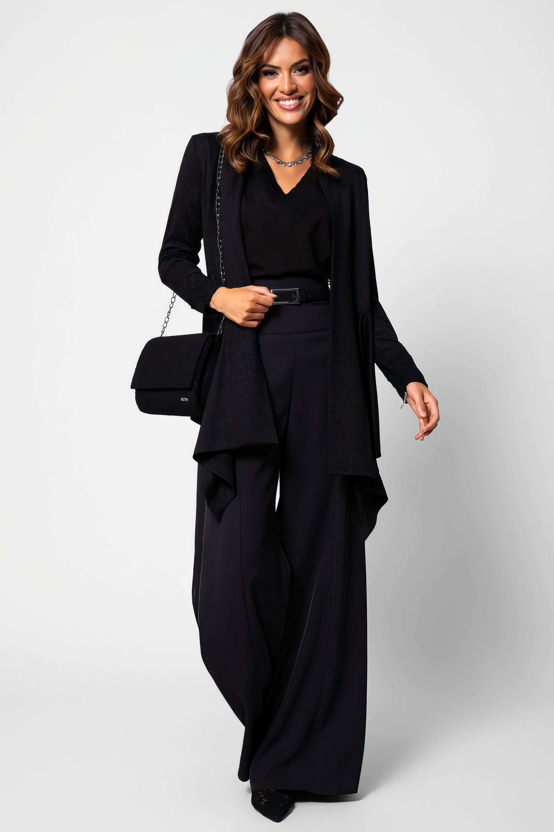Woman wearing Agatha High Waisted Wide Leg Pants in Black styled with a black top, belt, and long jacket.