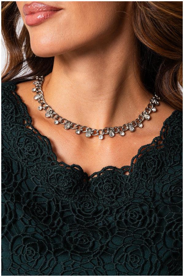 Close-up of a woman wearing the elegant blouse Midnight Green Jody Blouse with floral lace overlay and a silver charm necklace