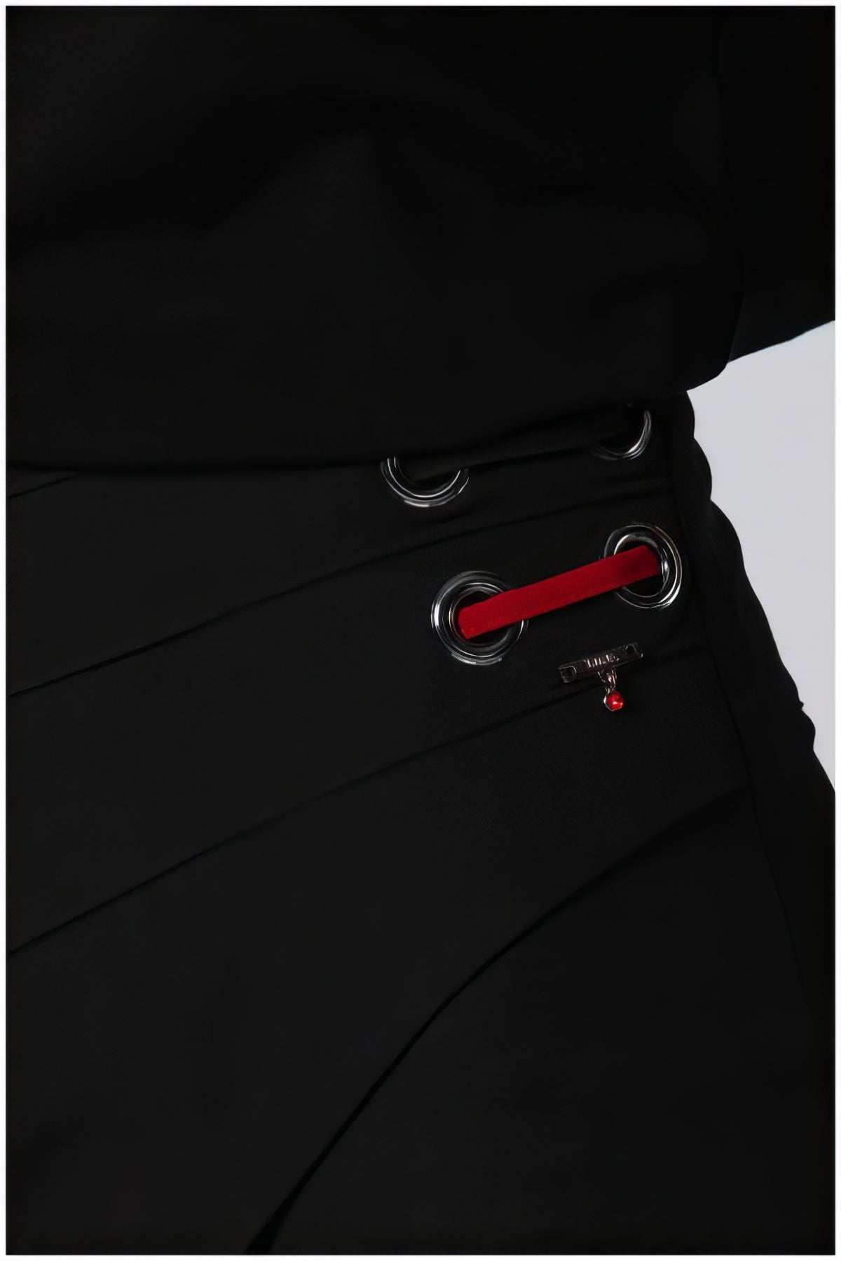 Close-up of Greta Wide Leg Pants in Black showing silver eyelets and a red lace detail for a refined look