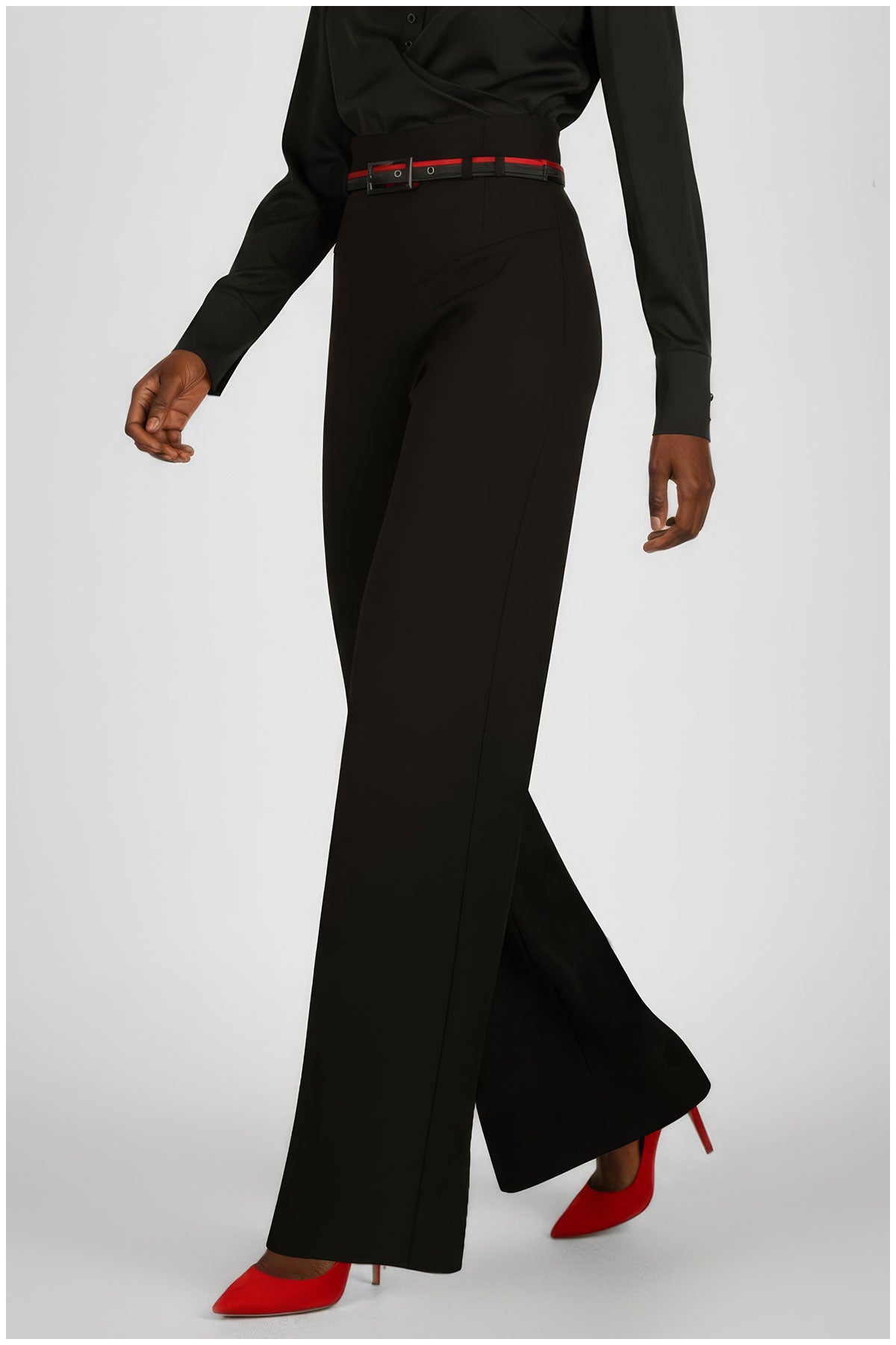 Person wearing black bell-bottom pants with a red belt and red shoes on a white background