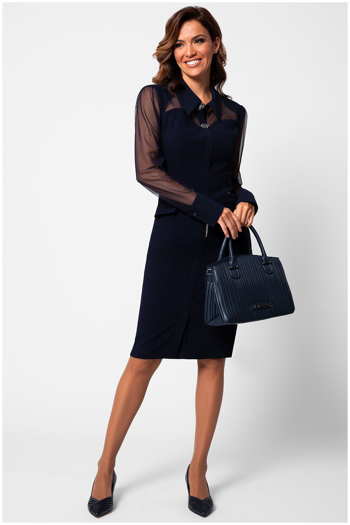 Woman wearing a black dress with sheer sleeves holding a matching handbag on a white background