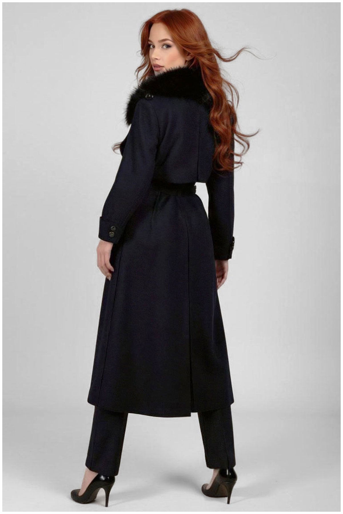 Woman wearing a long black coat with fur trim on a white background