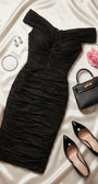 Black ruched cocktail midi styled on ivory satin with black patent pumps, mini handbag, crystal earrings, and a pink rose