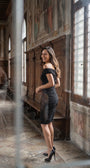 Woman wearing the black ruched off-shoulder cocktail midi in a historic interior corridor with carved columns and frescoes