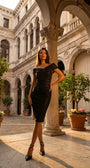 Model wearing the anthracite cocktail dress in a sunlit European courtyard with stone arches and citrus trees.
