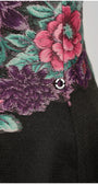Close-up of Rina floral dress showing cyclamen, purple, and teal embroidery with a small Luna button.