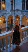 Rina black floral maxi dress in an old-world balcony setting with evening light.