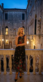 Rina black floral maxi dress worn on a historic balcony at blue hour with black heels.