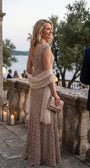 A woman in the beige lace gown looks back over her shoulder on a stone terrace by candlelight and water