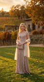 A woman in the beige lace gown at golden hour in a vineyard setting, styled with a soft wrap and clutch