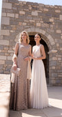 A woman in the beige lace gown stands beside a bride at a stone archway venue for a destination wedding