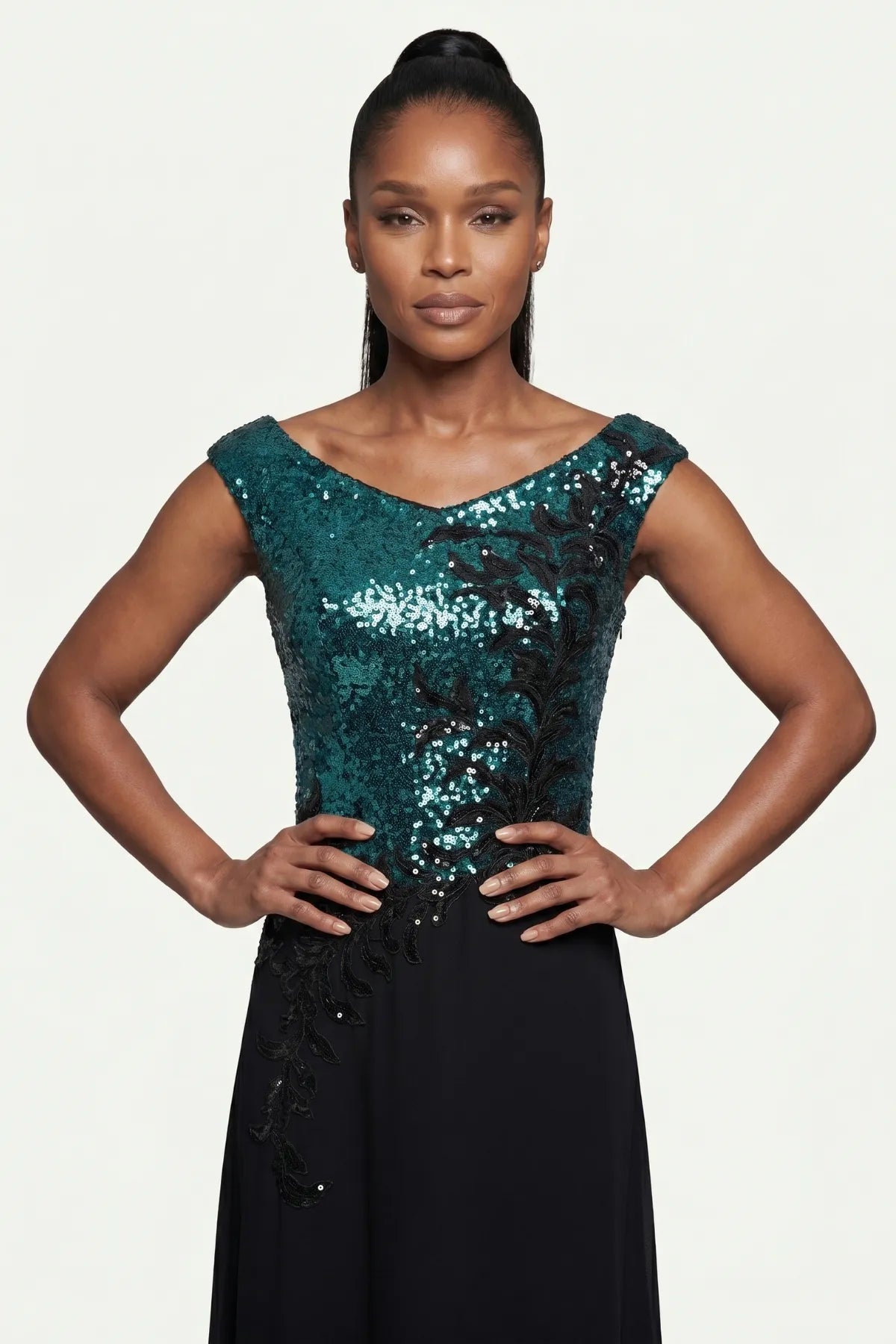 Close view of the teal sequined bodice, wide neckline, and black floral appliqué at the fitted waist