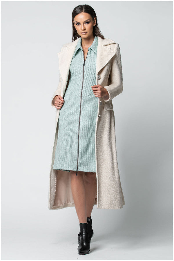 Woman wearing a long beige Luna Fashion House  coat over a light blue dress on a white background