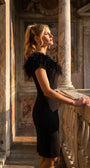 Model on a sunlit balcony in the dress with the feather collar attached, photographed in golden-hour light.