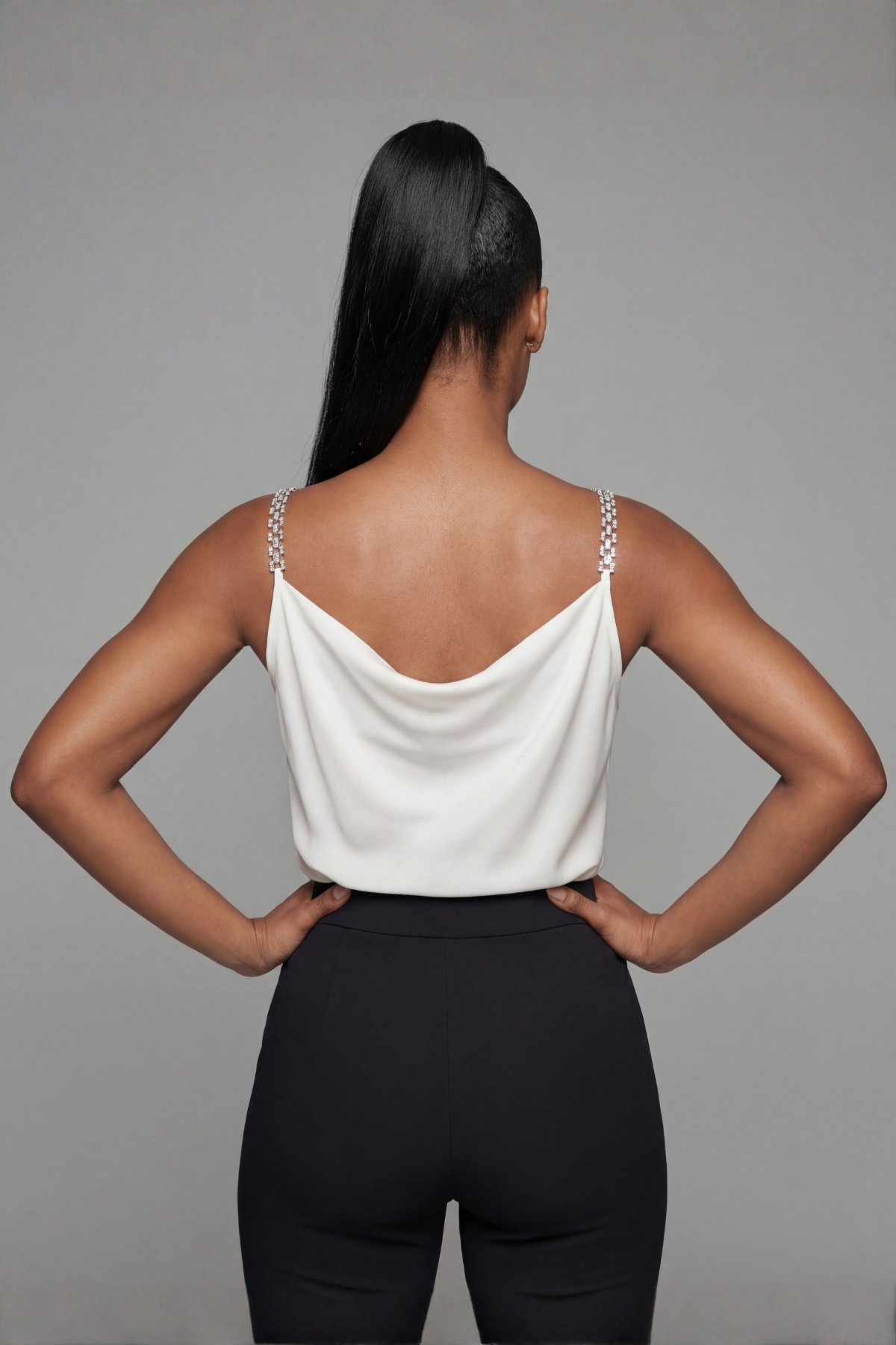 Person wearing a white sleeveless top and black pants against a gray background